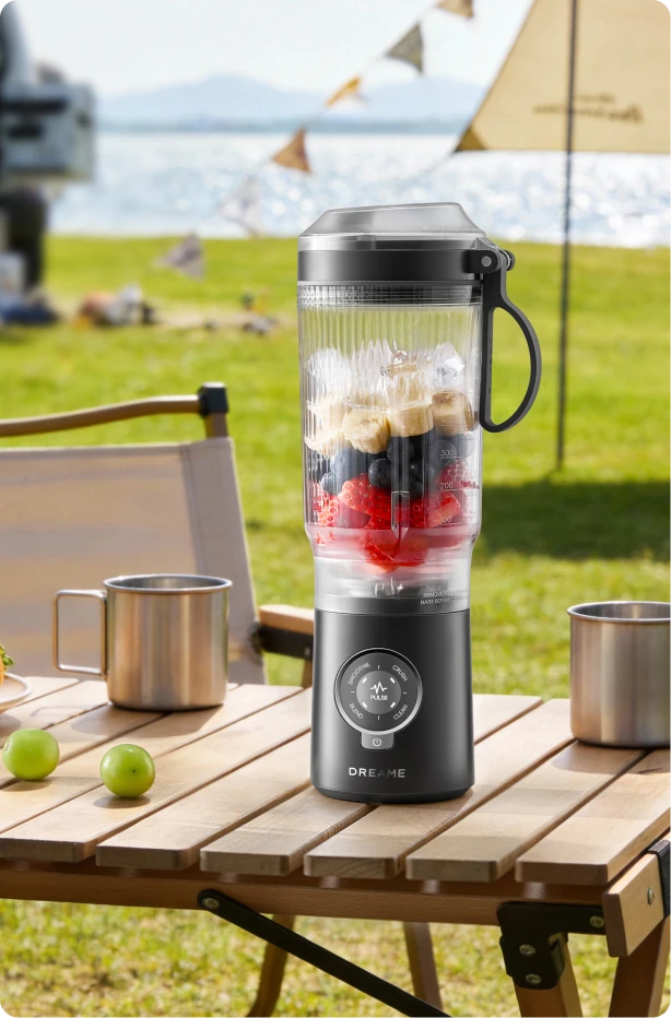 Dreame Portable Blender kabelloses Design auf einem Picknicktisch beim Mixen von Fruchtgetränken im Freien am Wasser
