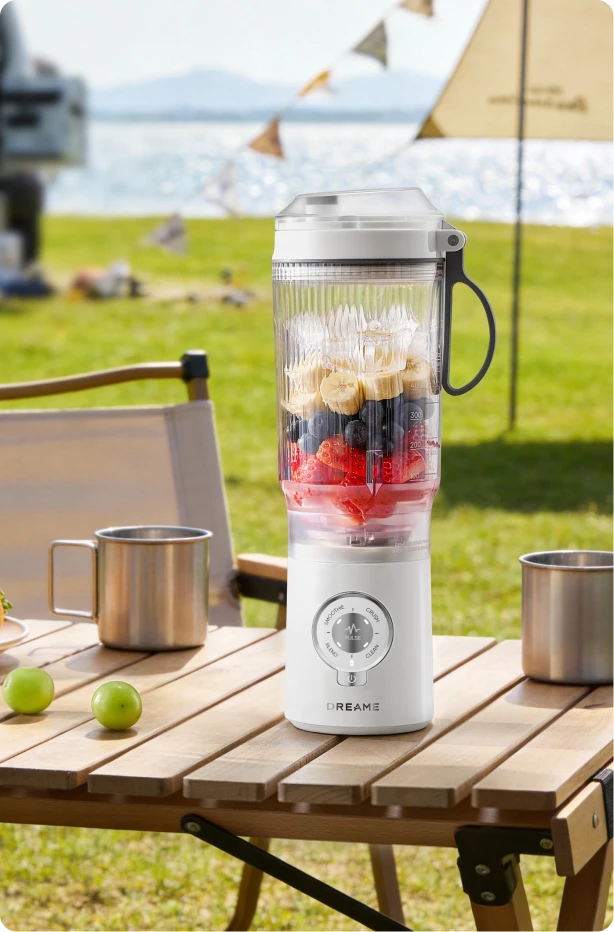 Dreame Portable Blender kabelloses Design auf einem Picknicktisch beim Mixen von Fruchtgetränken im Freien am Wasser